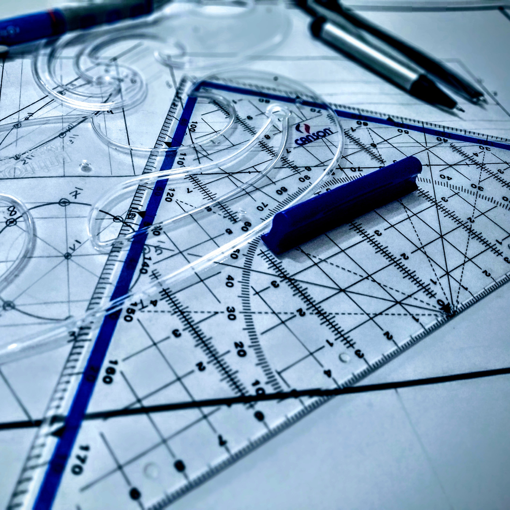Instrumentos de dibujo técnico sobre planos de ingeniería, incluyendo escuadras, reglas y lápices.